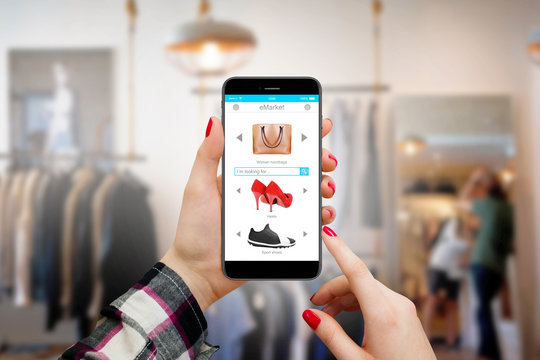 Women holding moder phone with shopping interface in hands inside clothing store and shopping online