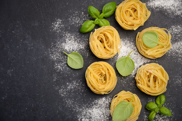 Raw tagliatelle pasta on the black concrete background, top view, copy space