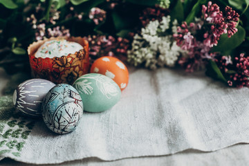 happy easter. easter cake and colorful decorated eggs on rustic background with lilac flowers.  egg with floral and chicken ornaments. space for text.  greeting card concept