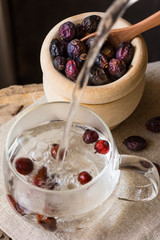 Pouring hot water to glass cup brewing rose hip tea, berried in wood bowl, linen towel, cozy atmosphere, natural medicine, holistic