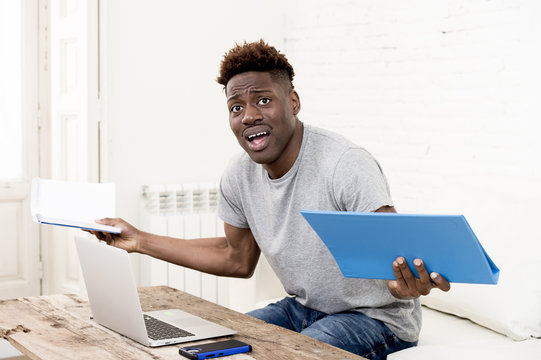 african american man sitting at home living room working with laptop computer and paperwork