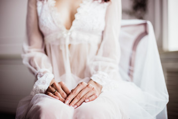 Fototapeta na wymiar beautiful girl in white transparent boudoir gown of tulle and lace sitting on a chair hands close-up