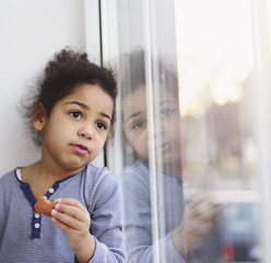 Sad little girl looking out the window. Her reflection in window shows her emotions.