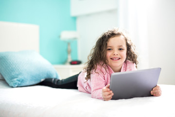 Technologies become easier. Cute little girl holding digital tablet and smiling while lying in bed.