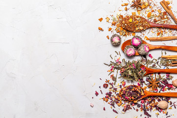 Dry tea in wooden spoons on grey background, top view. Leaves of red, fruit , green and black tea with  fruits and spices