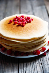 A stack of pancakes with cranberries on a white plate on a wooden boards background