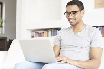 Browsing on the internet. full length shot of a smiling young afro American man using a laptop while relaxing in his living room at home.