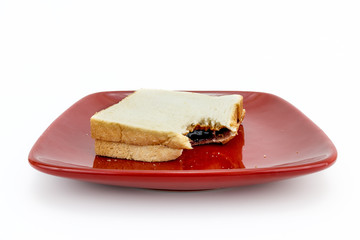 Peanut butter and jelly sandwich on plate with wite background.