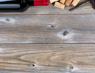 Top border of a bottle of red wine with vintage corkscrew and used corks on rustic wooden boards