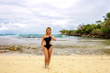 Fototapeta na wymiar Young happy girl in black bikini near the wild shore. Samana, Dominican Republic