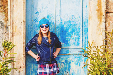 Outdoor fashion portrait of preteen 10-11 years old girl wearing blue leather jacket, hat and sunglasses