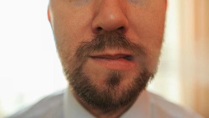 Obraz premium Young funny white businessman with beard and mustache emits puff of steam from the electronic cigarette in the kitchen. Close up.