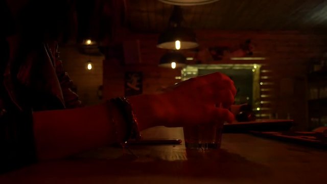 Pretty nice girl in restaurant holding a glass. Bar stand with drinks, menu, sign, glass. Red light and glow. Slow motion