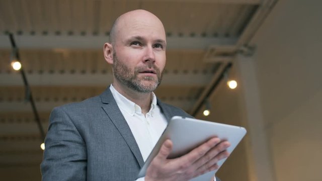Bald Middle-Aged Businessman Using a Tablet Computer