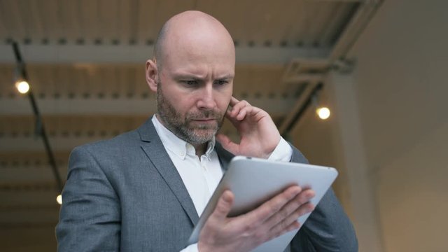 Bald Middle-Aged Businessman Using a Tablet Computer