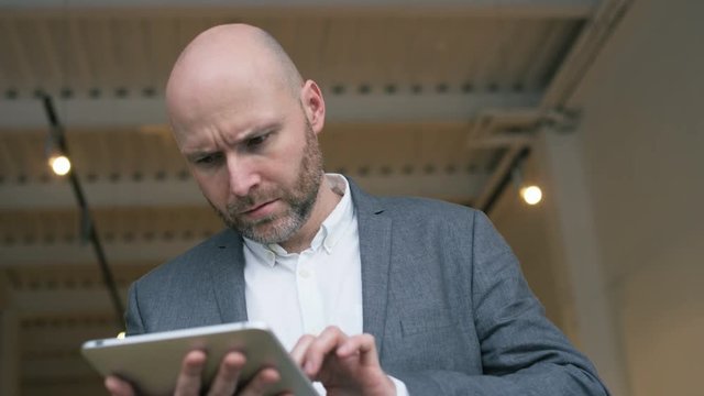 Bald Businessman Stops Using a Tablet Computer