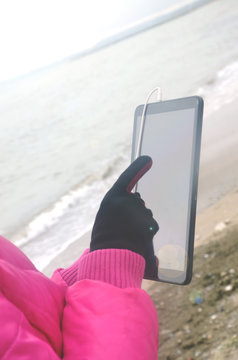 Hands with tablet near the ocean sea in cold weather