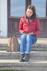 A beautiful young woman sitting on stairs and reading a book 