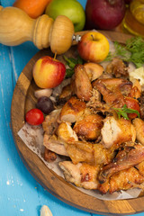 Whole roasted chicken garnished with tomatoes and apple on blue table.