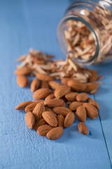 Almond in glass bottle and fresh nuts over blue background