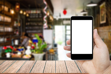 Mock up image of hand holding black mobile phone with blank white screen, Empty wood table top on blurred images coffee shop for background, perspective wood can be used for display products.
