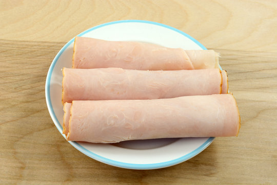 Rolls of smoked honey turkey breast meat on plate for snack or appetizer preparation