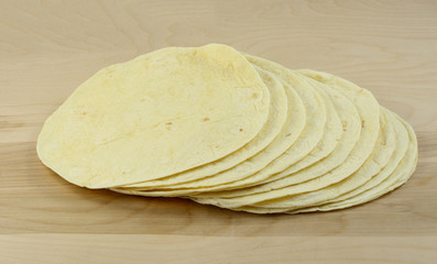 Four tortillas stacked up together on wooden table for dinner preparation
