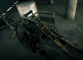 Fototapeta na wymiar one old wheelchair and old wooden crutches were forsaken in old room. lonely and scary concept. halloween theme