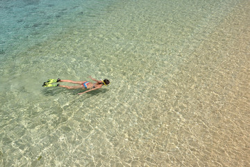 Woman in bikini is swimming with snorkel and fins in clean water.