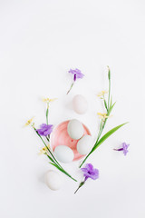 White Easter eggs in pink plate with yellow and purple  flowers on white background. Flat lay, top view. Traditional spring concept.