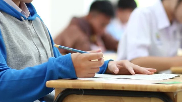 Asian group of young students and girl hands of student writing during test exam in classroom at high school in Thailand