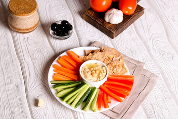 hummus served in a bowl with fresh vegetable sticks and whole grain crackers