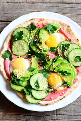 Vegetarian tortilla on a plate and on a wooden table. Easy and quick tortilla piled high with fried quail eggs, avocado, cucumbers, sesame seeds and parsley and lathered with beetroot hummus. Top view