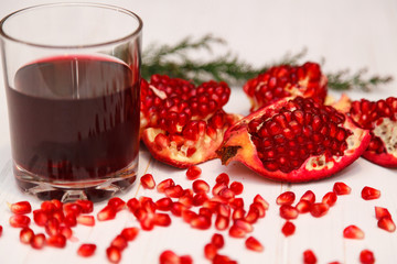 A glass of pomegranate juice and a pomegranate grain on a white wooden background