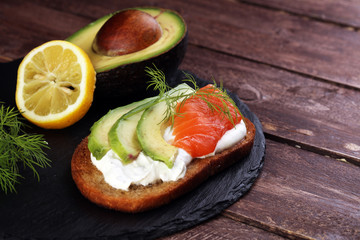 Bread with avocado and smoked salmon for lunch table. Sharing antipasti on party or summer picnic time over wooden rustic background.