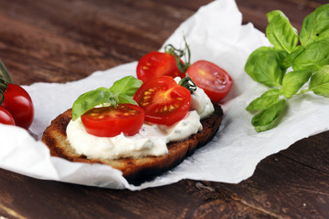 Bread with cream cheese and tomato for lunch table. Sharing antipasti on party or summer picnic time over wooden rustic background.