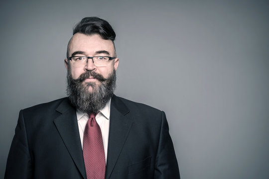 Adult bearded man in a suit and glasses on a gray background, toned