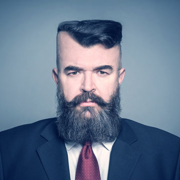 Adult angry bearded man in a suit with a square head on a gray background. Toned
