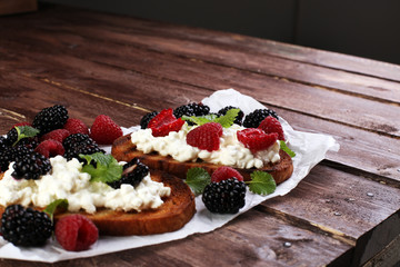 Bread with cheese cream and blackberries and raspberries for lunch table. Sharing antipasti on party or summer picnic time over wooden rustic background.