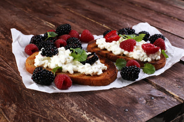 Bread with cheese cream and blackberries and raspberries for lunch table. Sharing antipasti on party or summer picnic time over wooden rustic background.