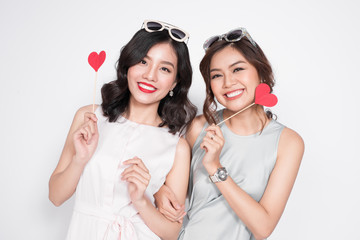 Two fashionable women in nice dresses standing together and holding red heart shape.