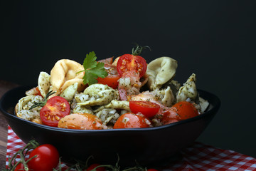 Bowl of tricolor tortellini pasta salad with tomatoes and onions on dark wood table background