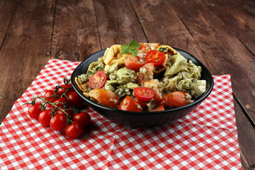 Bowl of tricolor tortellini pasta salad with tomatoes and onions on dark wood table background