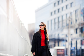 Fashionable young woman walking in street in the city She wears sunglasses, black shirt and jacket .