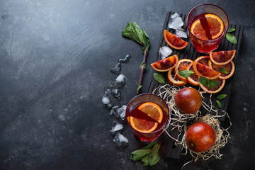 Blood oranges juice with fresh mint leaves and ice on a dark stone background, high angle view, copyspace