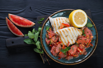 Top view of grilled calamari with fresh grapefruit salad on a black wooden background