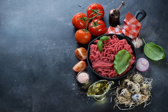 Raw ground beef meat and various cooking components on a dark metal background, high angle view with copyspace