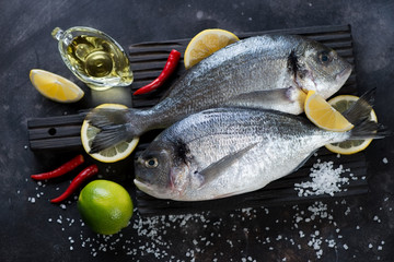 Couple of fresh uncooked sea breams with seasonings on a black wooden cutting board, studio shot
