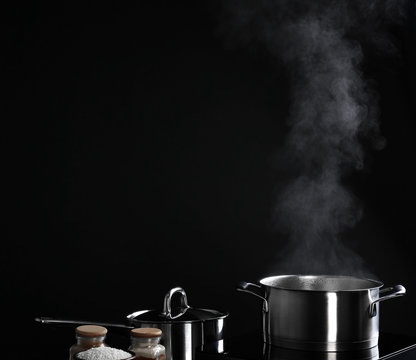 Saucepan with steam on black background