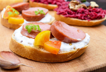 Sandwiches for breakfast with fried sausages, yellow tomatoes, creamy mustard sauce on a cutting board.